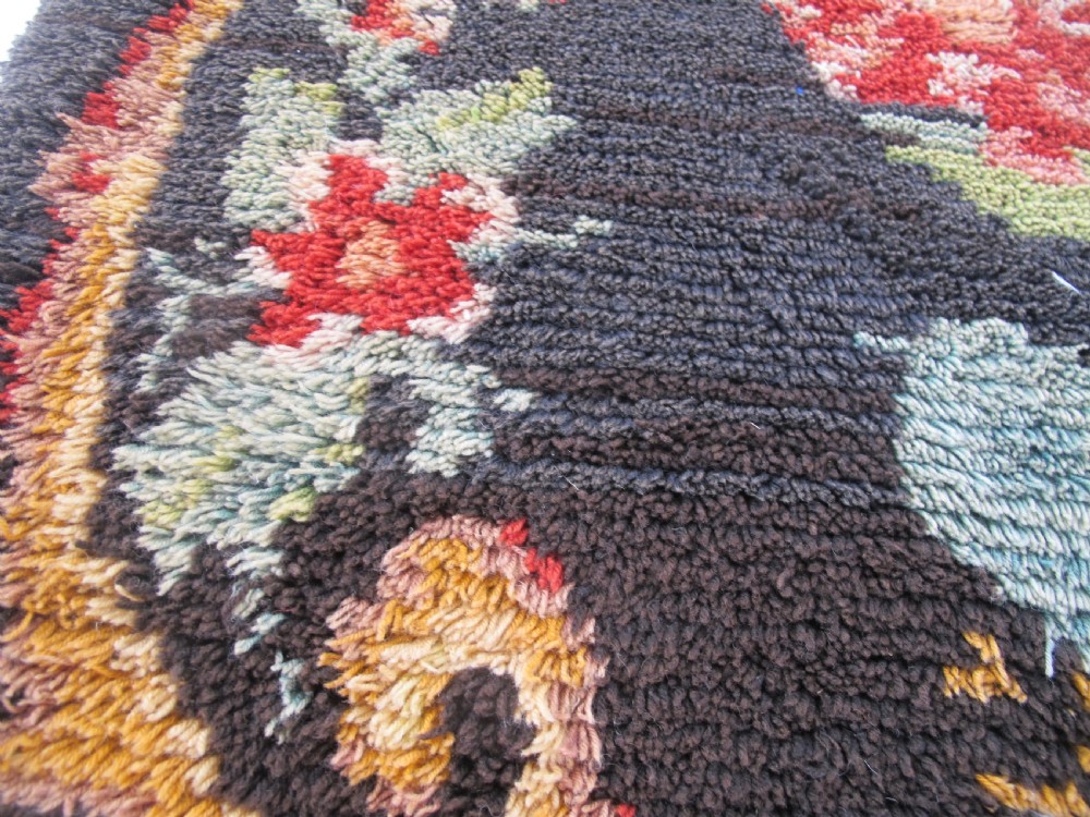 An early 20th-century Scandinavian Rya wool rug featuring a central floral bouquet in yellow, red, and green with scrollwork borders on a black field. View IX