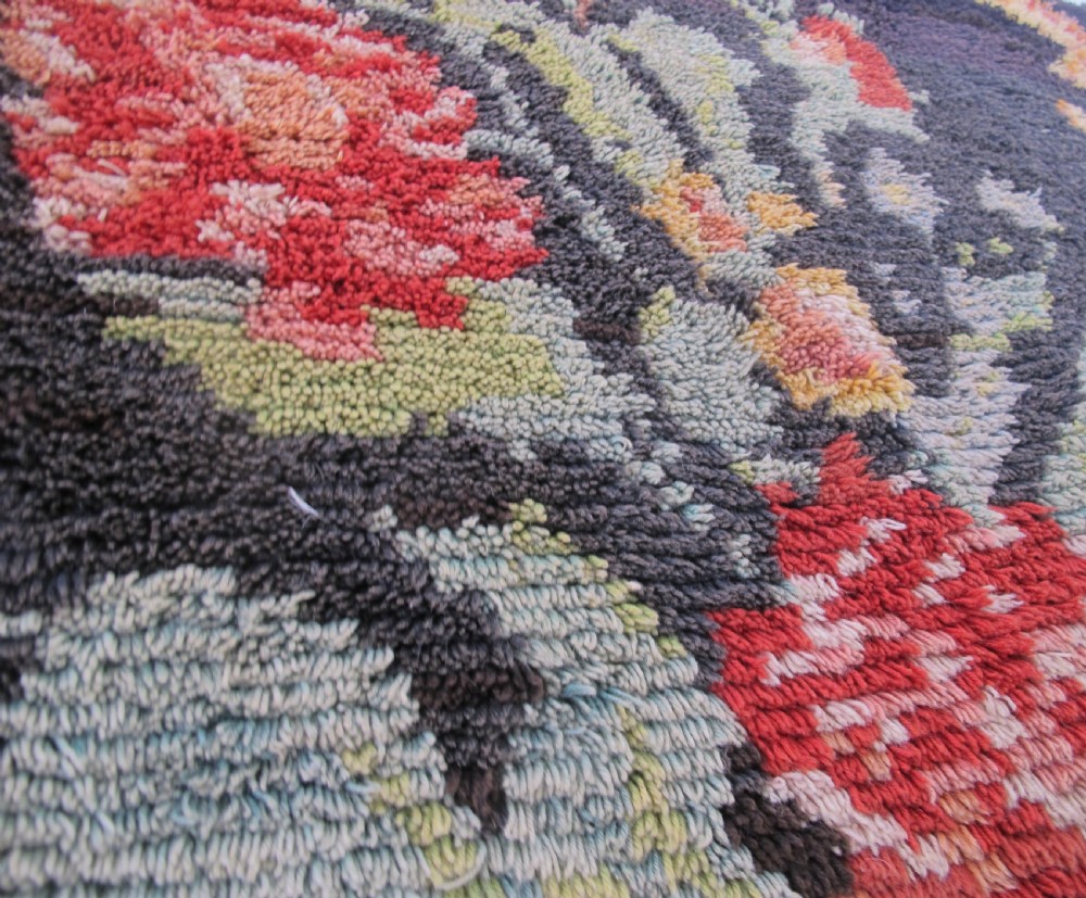 An early 20th-century Scandinavian Rya wool rug featuring a central floral bouquet in yellow, red, and green with scrollwork borders on a black field. View X