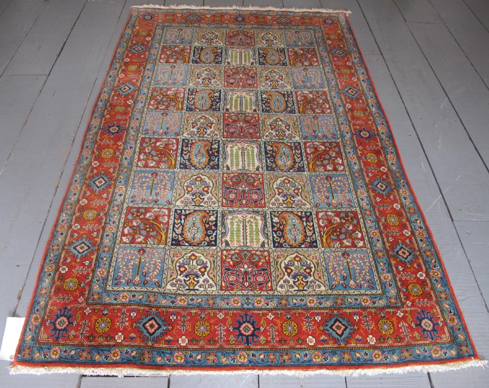 A rectangular hand-knotted Persian Qum rug featuring a central field of grid compartments filled with botanical and cypress motifs framed by a red border.