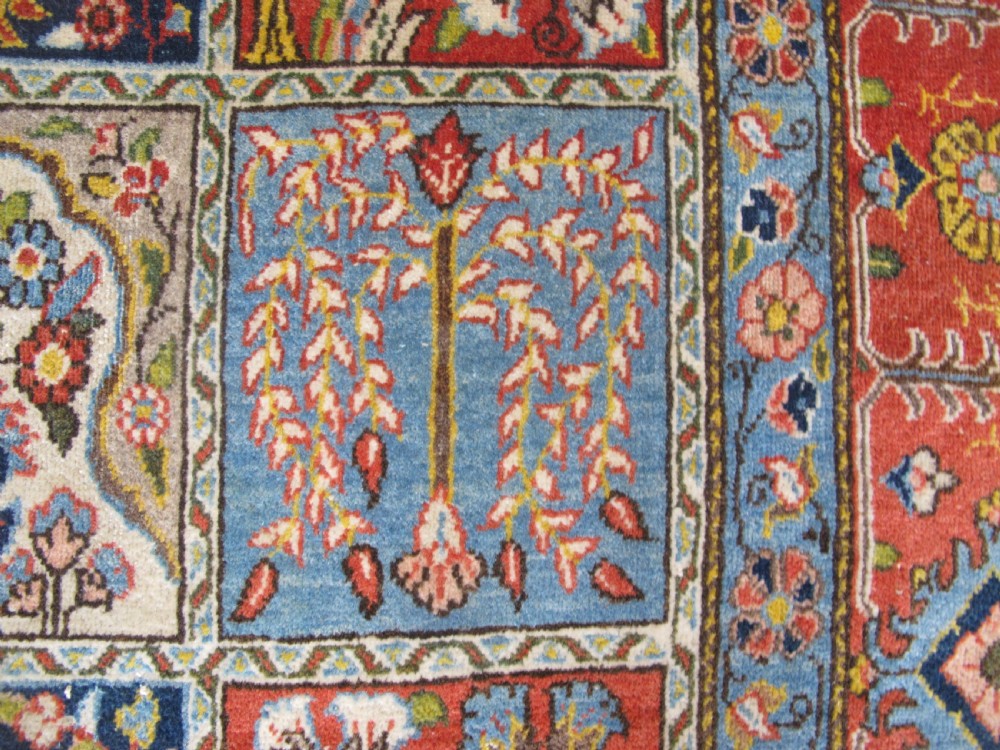 A rectangular hand-knotted Persian Qum rug featuring a central field of grid compartments filled with botanical and cypress motifs framed by a red border. View X