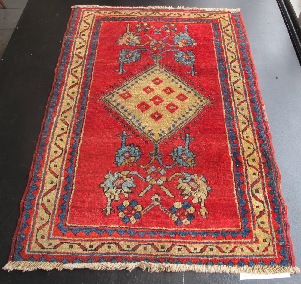 A small hand-knotted North-West Persian wool rug with a central gold diamond medallion surrounded by geometric floral motifs on a vibrant red field with multi-coloured borders.