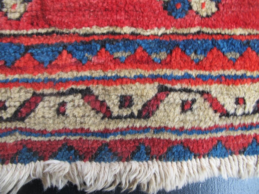A small hand-knotted North-West Persian wool rug with a central gold diamond medallion surrounded by geometric floral motifs on a vibrant red field with multi-coloured borders. View III