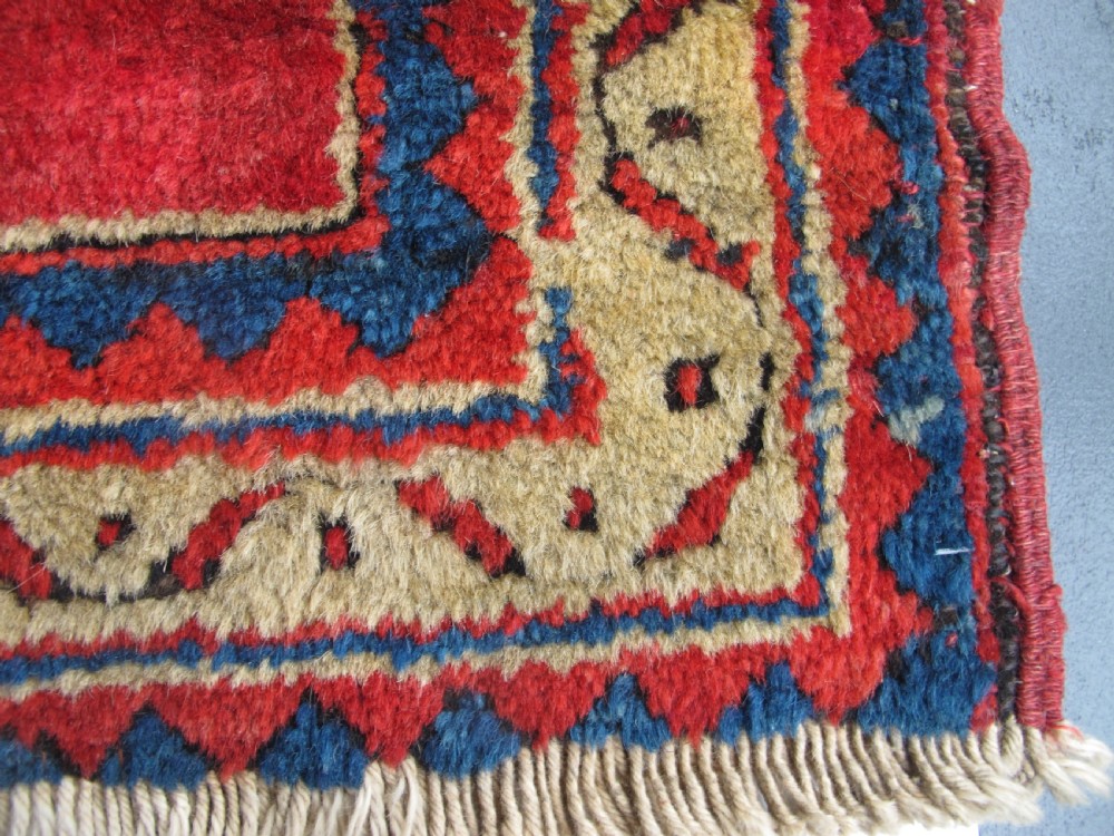 A small hand-knotted North-West Persian wool rug with a central gold diamond medallion surrounded by geometric floral motifs on a vibrant red field with multi-coloured borders. View IV