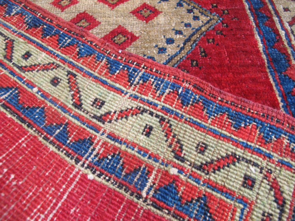 A small hand-knotted North-West Persian wool rug with a central gold diamond medallion surrounded by geometric floral motifs on a vibrant red field with multi-coloured borders. View VIII
