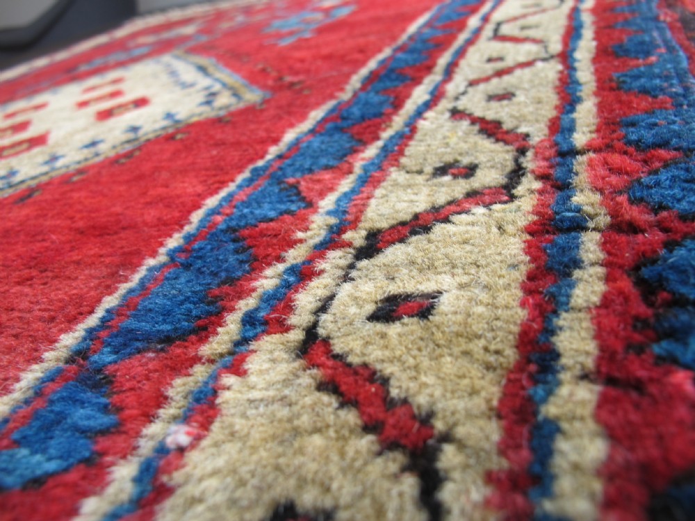 A small hand-knotted North-West Persian wool rug with a central gold diamond medallion surrounded by geometric floral motifs on a vibrant red field with multi-coloured borders. View X