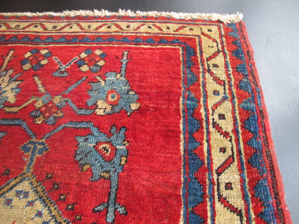 A small hand-knotted North-West Persian wool rug with a central gold diamond medallion surrounded by geometric floral motifs on a vibrant red field with multi-coloured borders. View XI