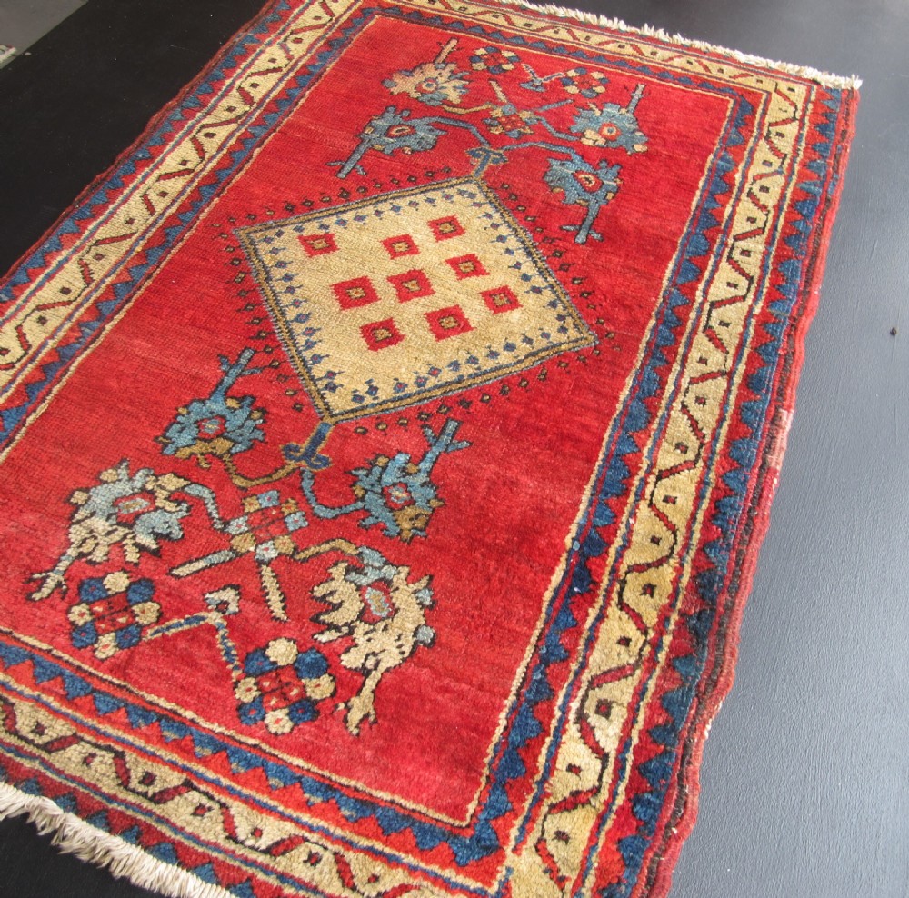 A small hand-knotted North-West Persian wool rug with a central gold diamond medallion surrounded by geometric floral motifs on a vibrant red field with multi-coloured borders. View XII