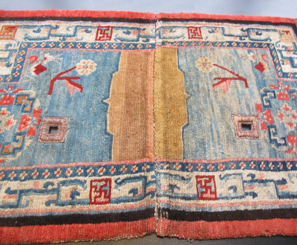 A hand-knotted wool Tibetan saddle cover featuring a blue central field with floral motifs, geometric inner borders, a red outer margin, and leather-bound stirrup slots. View VIII