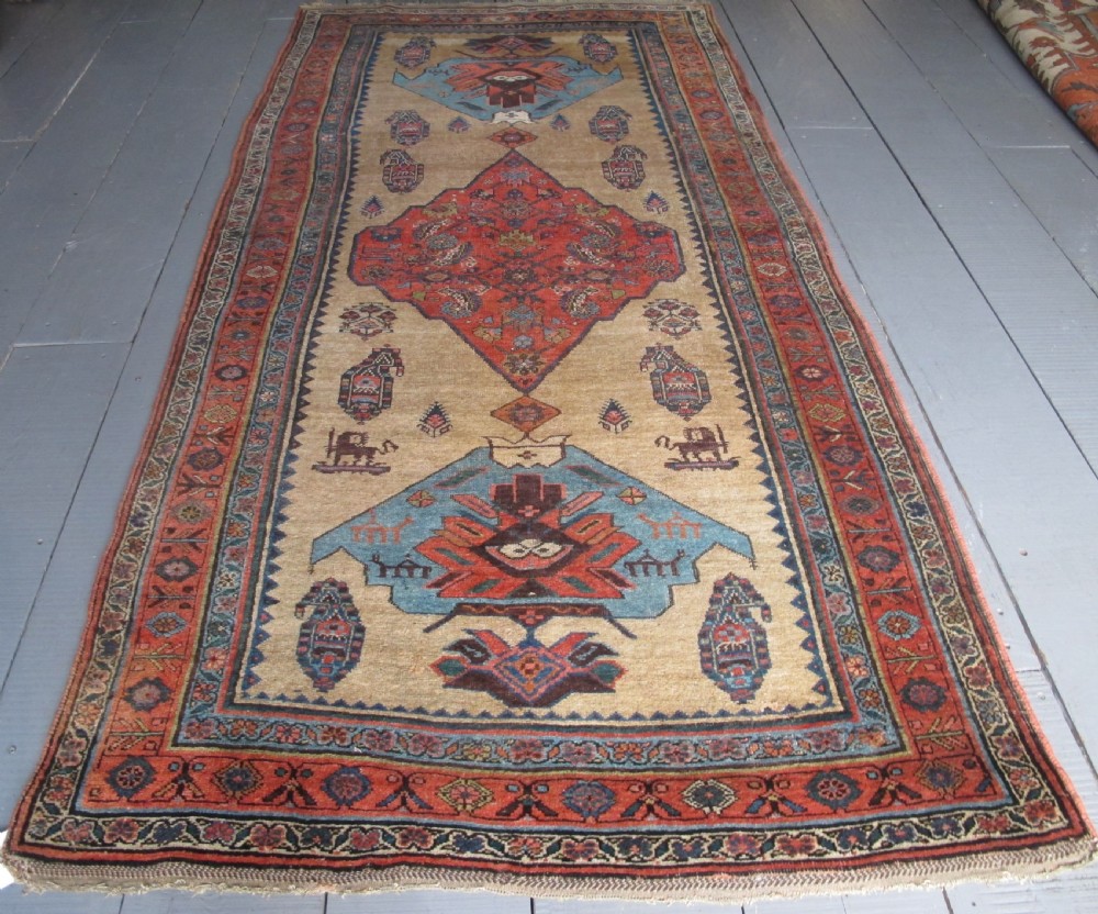 An antique hand-knotted wool long rug featuring a central red diamond medallion on a camel field framed by blue spandrels and multi-banded borders.