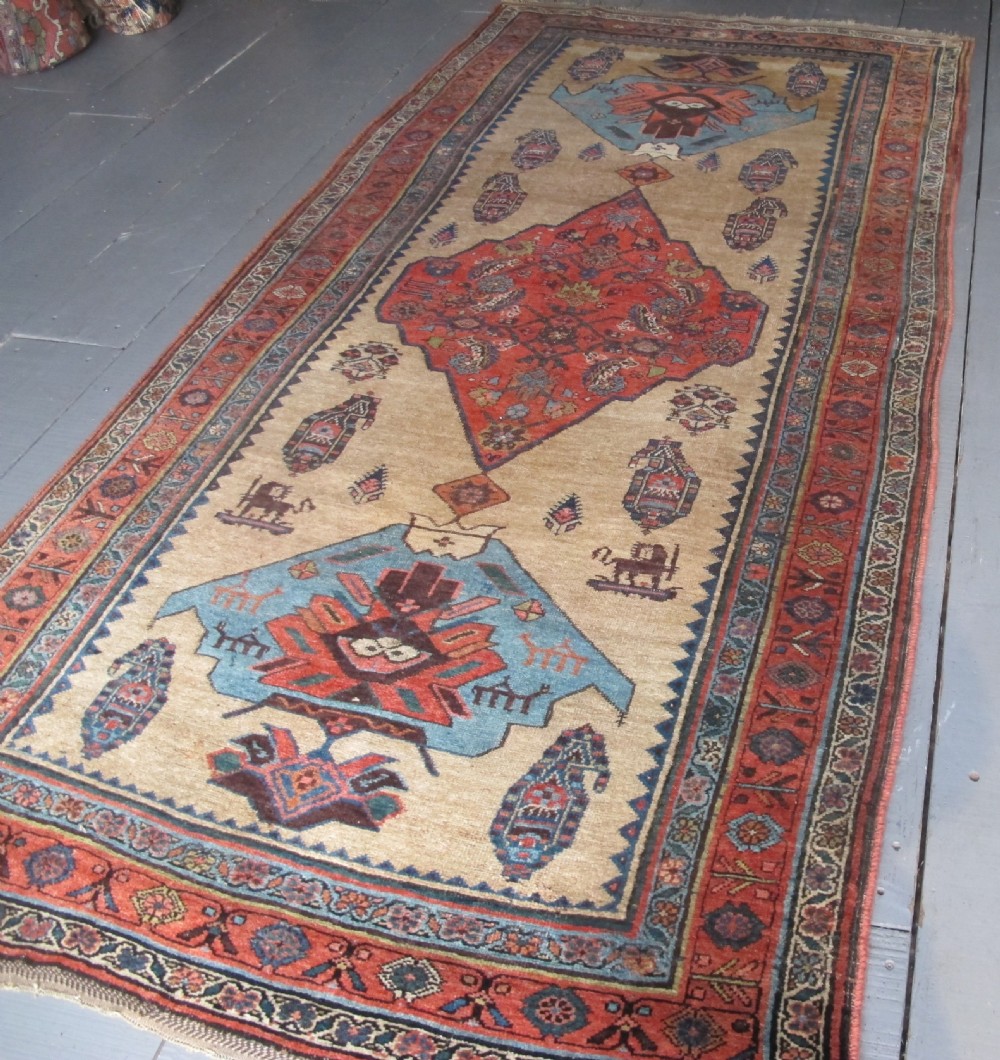 An antique hand-knotted wool long rug featuring a central red diamond medallion on a camel field framed by blue spandrels and multi-banded borders. View II