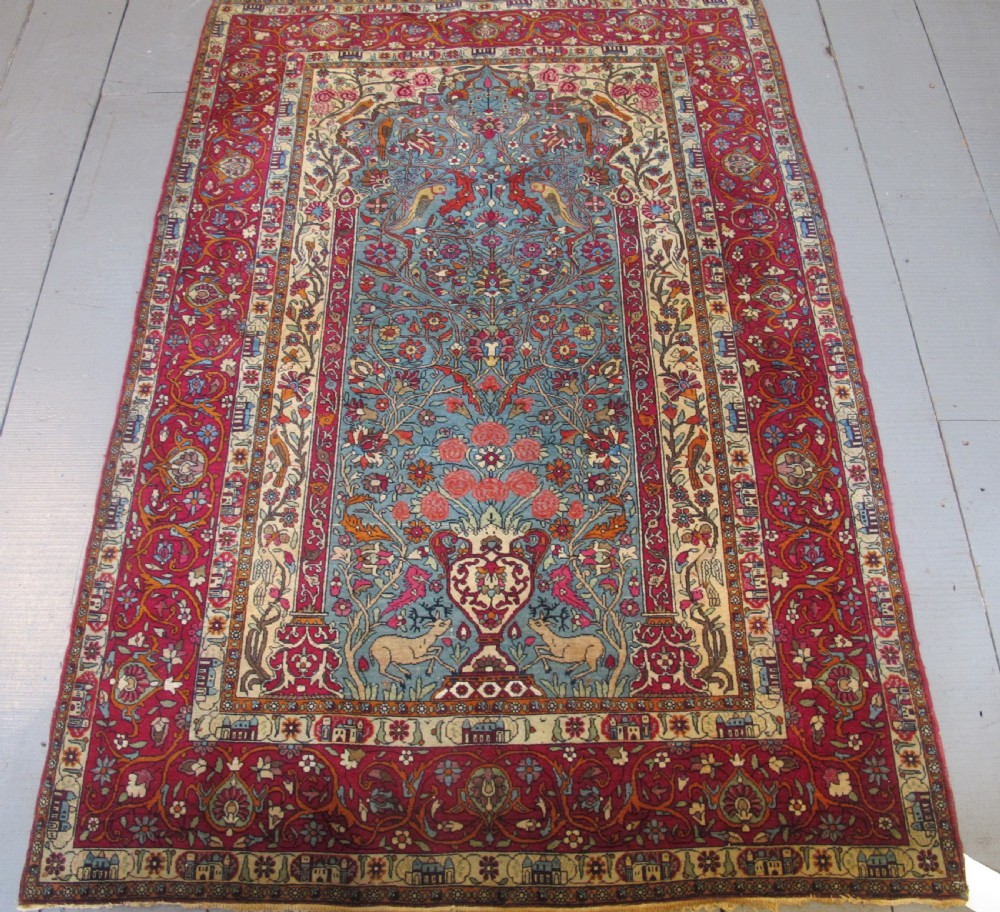 An antique Persian Isfahan hand-knotted wool rug featuring a light blue field with a vase and floral tree motif flanked by deer, framed by a red floral border.