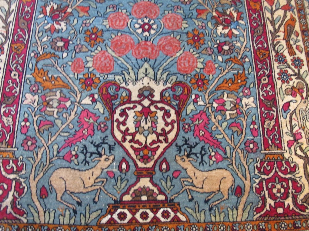 An antique Persian Isfahan hand-knotted wool rug featuring a light blue field with a vase and floral tree motif flanked by deer, framed by a red floral border. View II