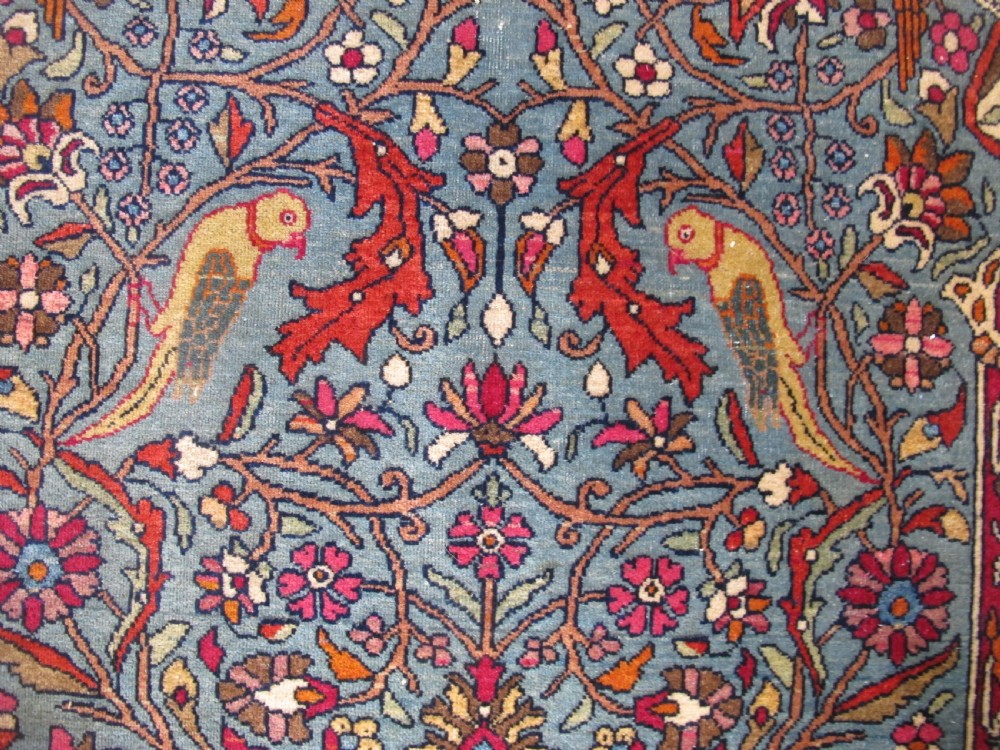 An antique Persian Isfahan hand-knotted wool rug featuring a light blue field with a vase and floral tree motif flanked by deer, framed by a red floral border. View III