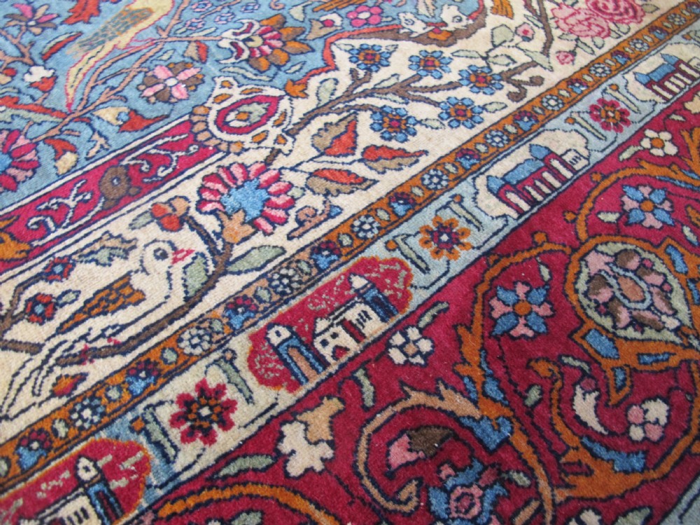An antique Persian Isfahan hand-knotted wool rug featuring a light blue field with a vase and floral tree motif flanked by deer, framed by a red floral border. View X