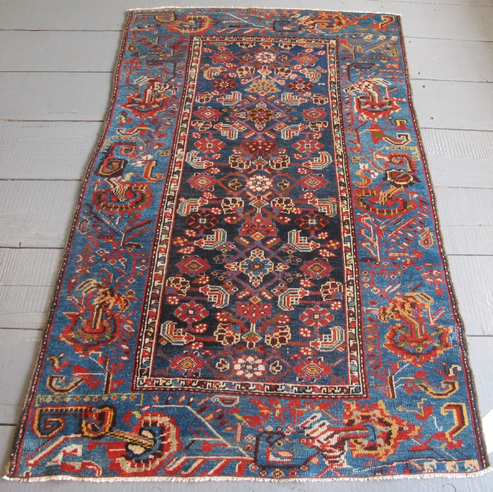 A late 19th-century hand-knotted Persian Hamadan wool rug featuring a dark navy central field surrounded by vibrant blue and red borders with intricate geometric floral motifs.