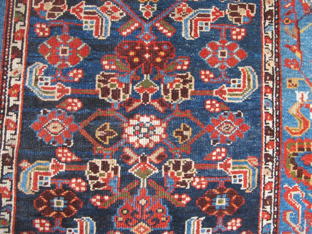A late 19th-century hand-knotted Persian Hamadan wool rug featuring a dark navy central field surrounded by vibrant blue and red borders with intricate geometric floral motifs. View X