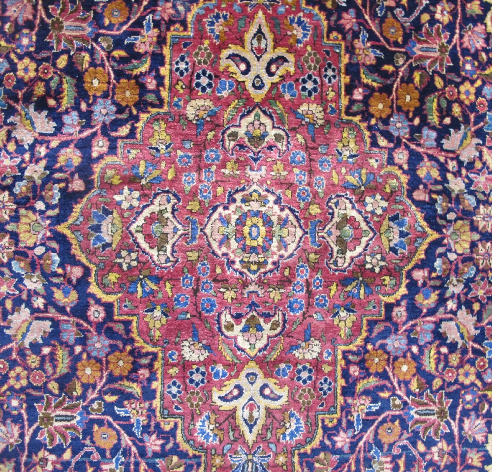 An antique central Persian silk Kashan rug featuring an intricate central medallion surrounded by floral motifs in crimson, navy blue, and gold tones. View II