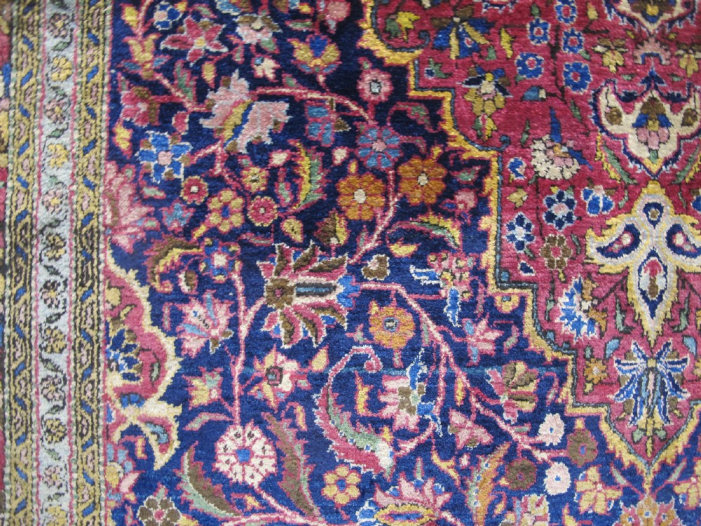 An antique central Persian silk Kashan rug featuring an intricate central medallion surrounded by floral motifs in crimson, navy blue, and gold tones. View III