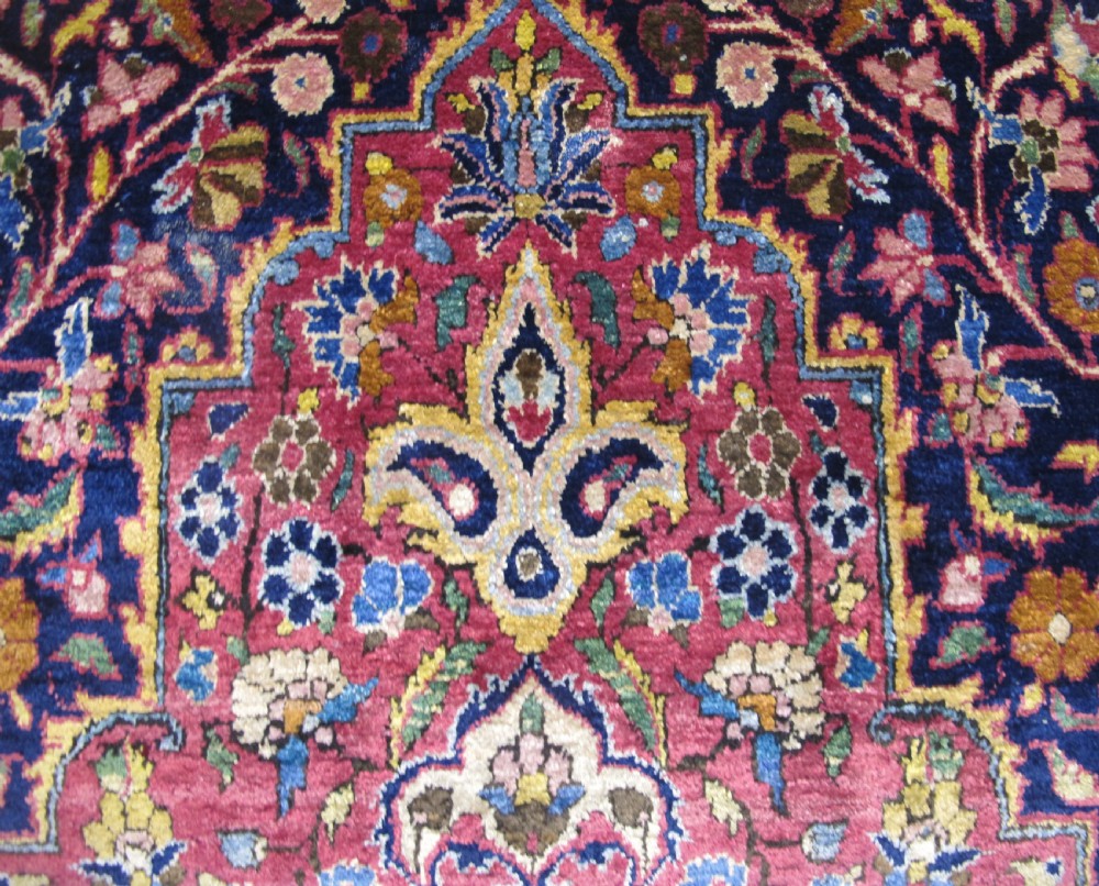 An antique central Persian silk Kashan rug featuring an intricate central medallion surrounded by floral motifs in crimson, navy blue, and gold tones. View V