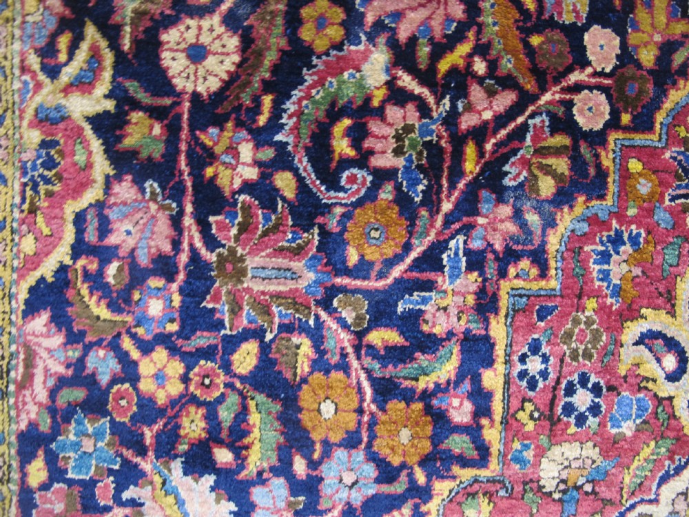 An antique central Persian silk Kashan rug featuring an intricate central medallion surrounded by floral motifs in crimson, navy blue, and gold tones. View VI