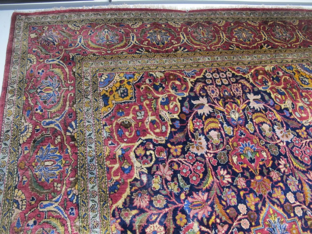 An antique central Persian silk Kashan rug featuring an intricate central medallion surrounded by floral motifs in crimson, navy blue, and gold tones. View VII