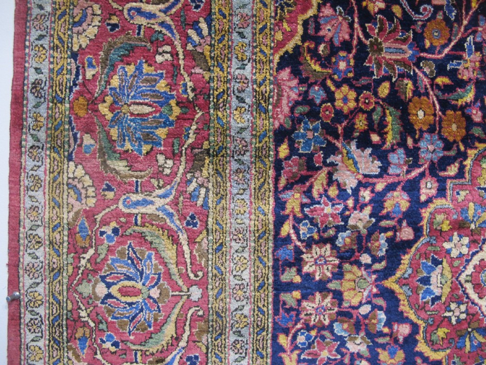 An antique central Persian silk Kashan rug featuring an intricate central medallion surrounded by floral motifs in crimson, navy blue, and gold tones. View IX