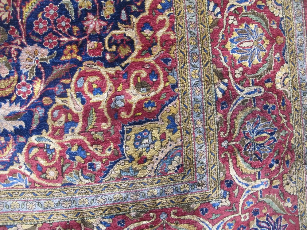 An antique central Persian silk Kashan rug featuring an intricate central medallion surrounded by floral motifs in crimson, navy blue, and gold tones. View X