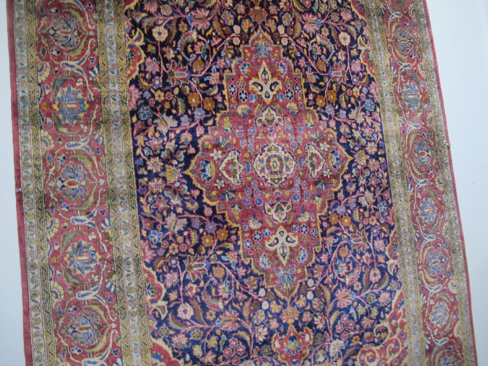 An antique central Persian silk Kashan rug featuring an intricate central medallion surrounded by floral motifs in crimson, navy blue, and gold tones. View XII