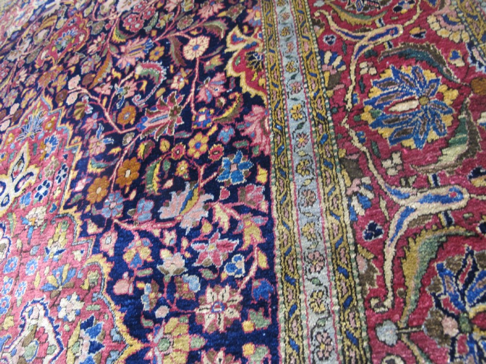 An antique central Persian silk Kashan rug featuring an intricate central medallion surrounded by floral motifs in crimson, navy blue, and gold tones. View XIII