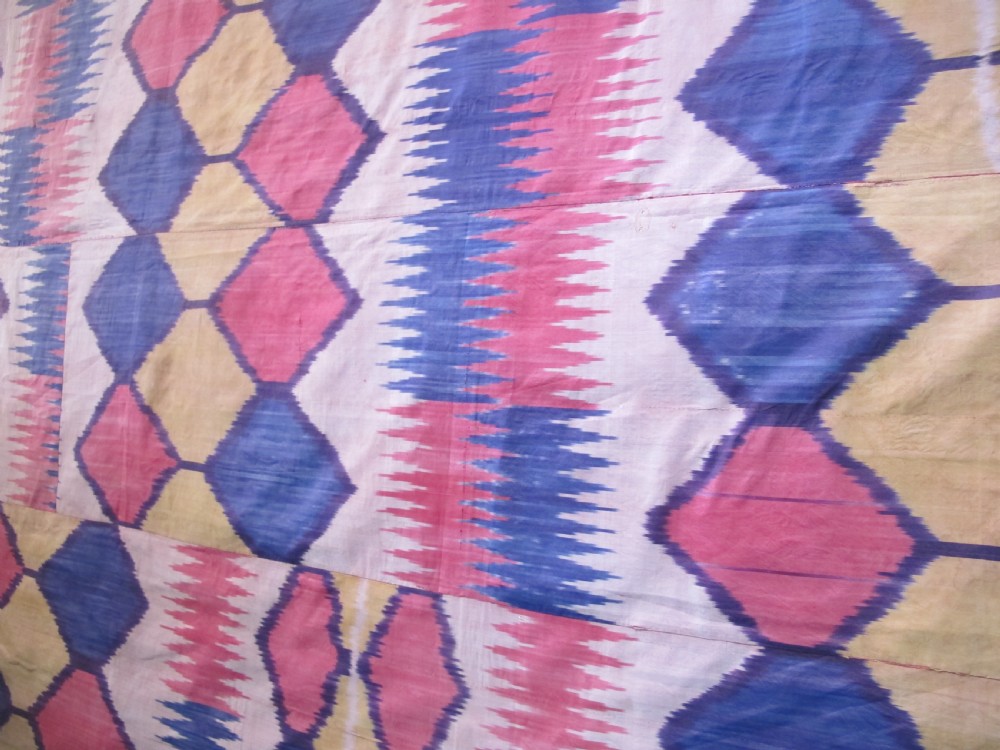 A large handwoven silk ikat textile panel from Uzbekistan featuring geometric diamond motifs and sawtooth patterns in pink, yellow, and purple. View II