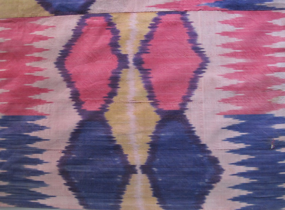 A large handwoven silk ikat textile panel from Uzbekistan featuring geometric diamond motifs and sawtooth patterns in pink, yellow, and purple. View III