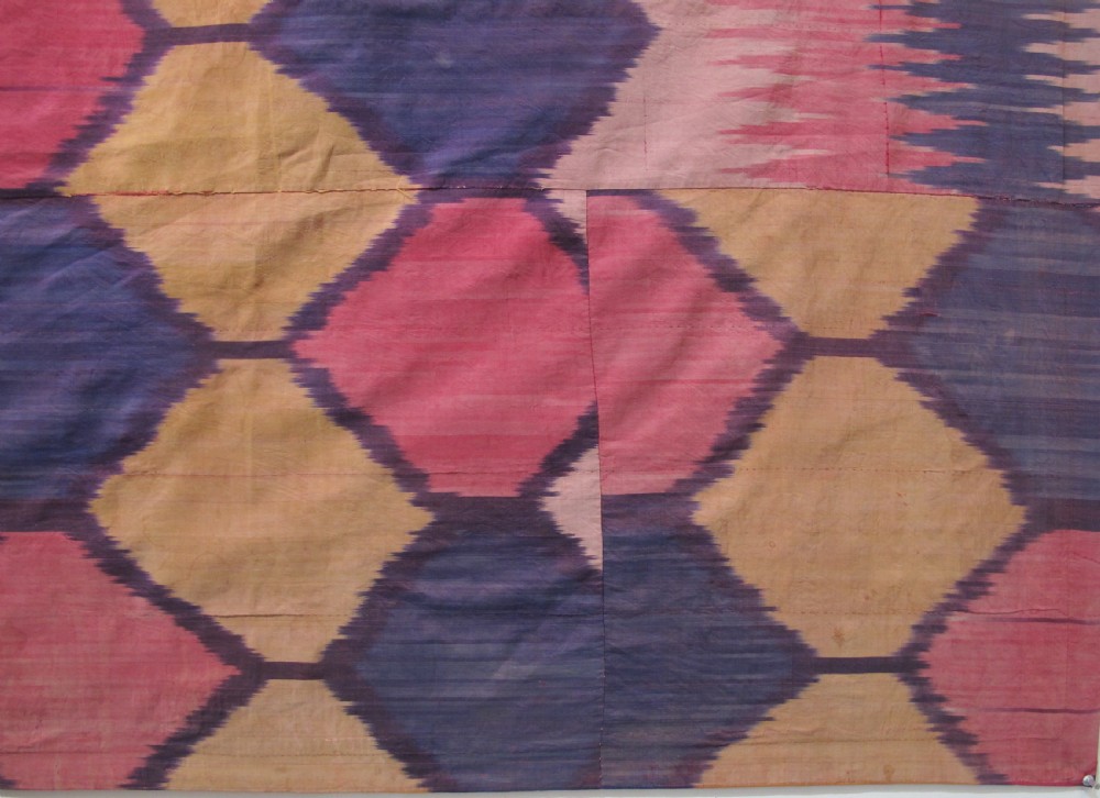 A large handwoven silk ikat textile panel from Uzbekistan featuring geometric diamond motifs and sawtooth patterns in pink, yellow, and purple. View IV