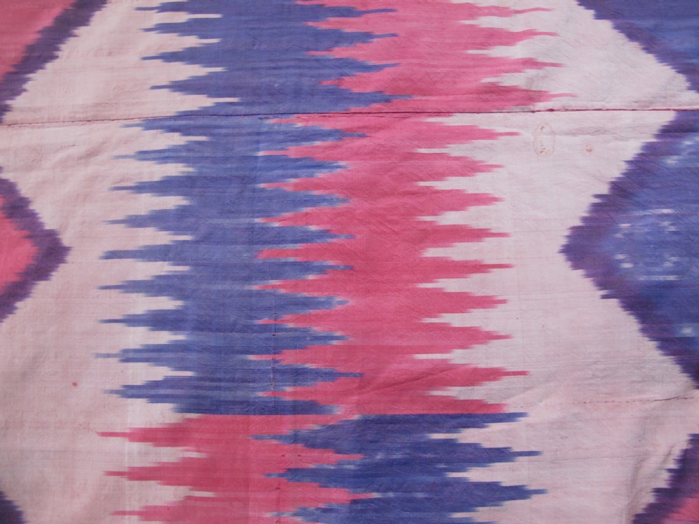A large handwoven silk ikat textile panel from Uzbekistan featuring geometric diamond motifs and sawtooth patterns in pink, yellow, and purple. View V
