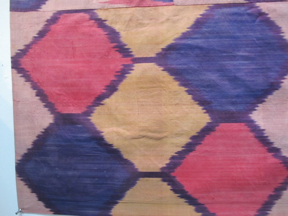 A large handwoven silk ikat textile panel from Uzbekistan featuring geometric diamond motifs and sawtooth patterns in pink, yellow, and purple. View VII