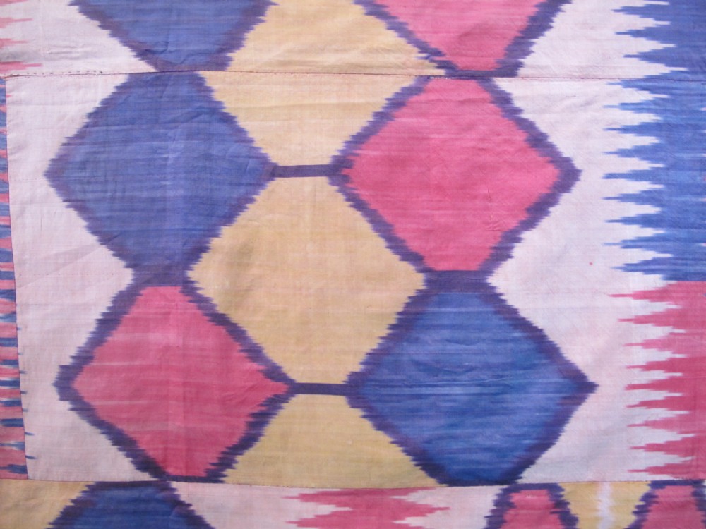 A large handwoven silk ikat textile panel from Uzbekistan featuring geometric diamond motifs and sawtooth patterns in pink, yellow, and purple. View IX
