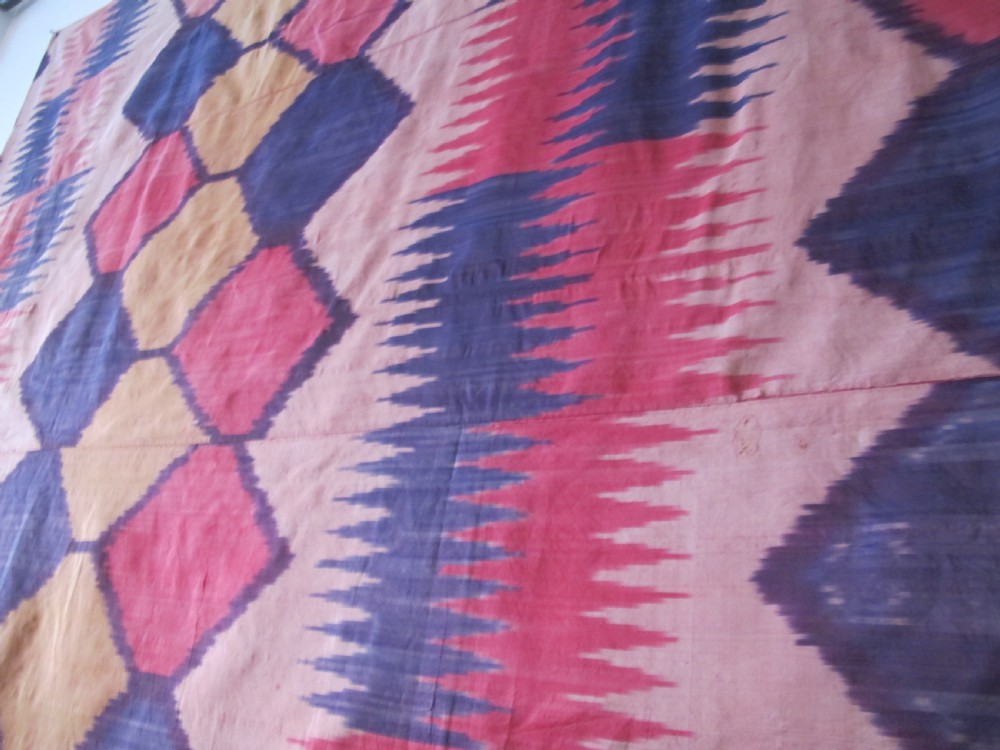 A large handwoven silk ikat textile panel from Uzbekistan featuring geometric diamond motifs and sawtooth patterns in pink, yellow, and purple. View X