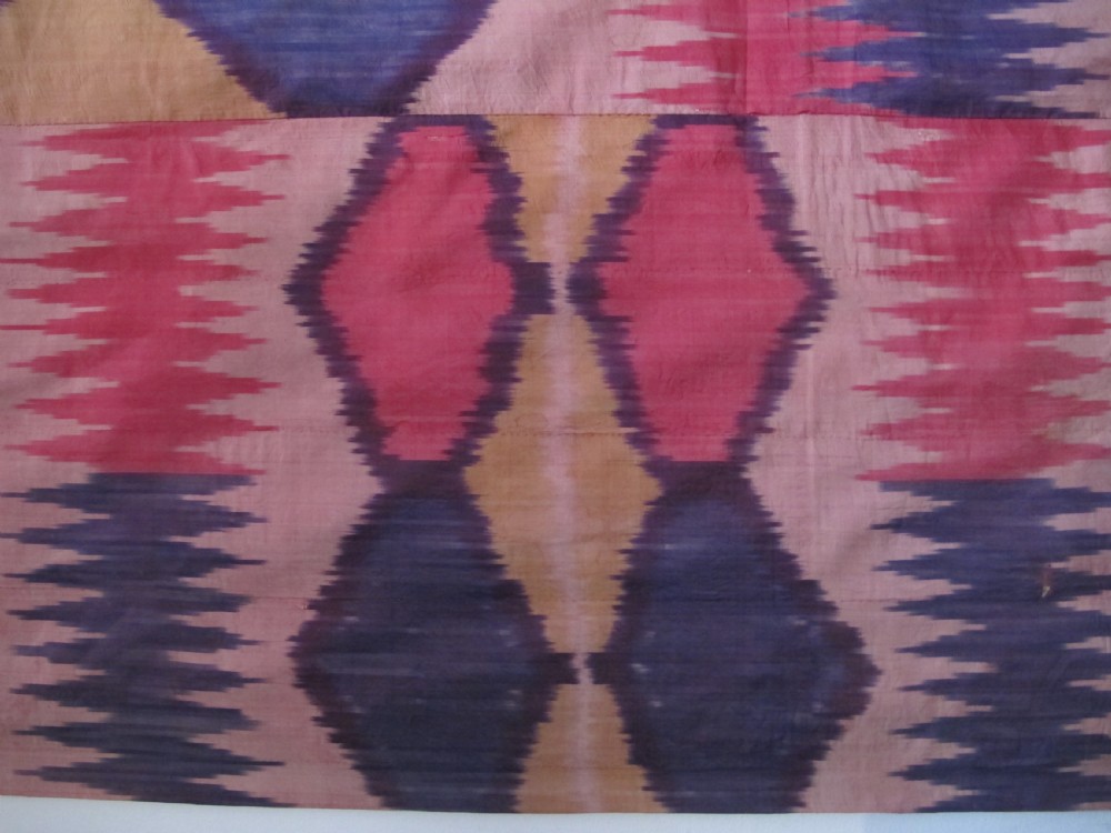 A large handwoven silk ikat textile panel from Uzbekistan featuring geometric diamond motifs and sawtooth patterns in pink, yellow, and purple. View XI