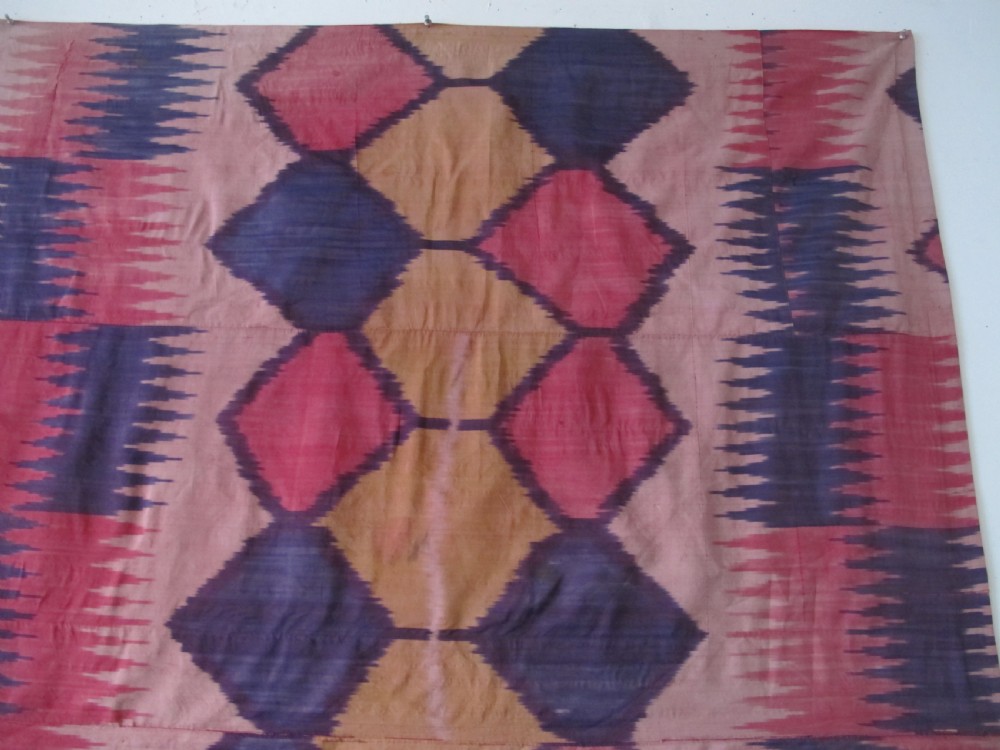 A large handwoven silk ikat textile panel from Uzbekistan featuring geometric diamond motifs and sawtooth patterns in pink, yellow, and purple. View XII