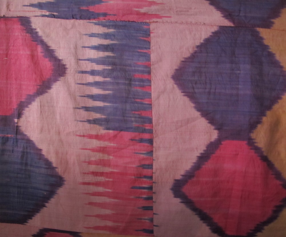 A large handwoven silk ikat textile panel from Uzbekistan featuring geometric diamond motifs and sawtooth patterns in pink, yellow, and purple. View XIV