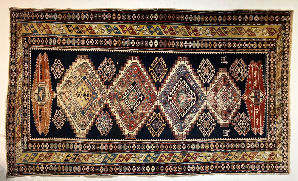 A rectangular hand-knotted wool rug displaying four diamond medallions along a navy central field surrounded by multi-tiered geometric borders.