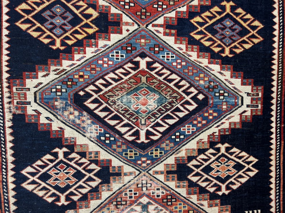 A rectangular hand-knotted wool rug displaying four diamond medallions along a navy central field surrounded by multi-tiered geometric borders. View III