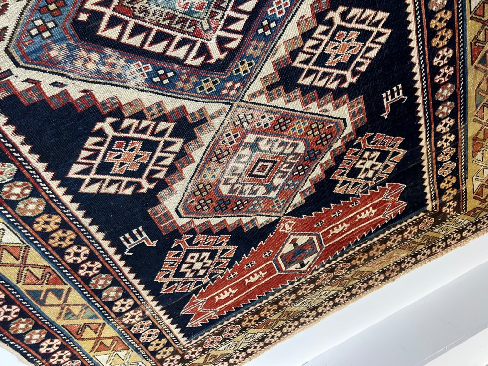 A rectangular hand-knotted wool rug displaying four diamond medallions along a navy central field surrounded by multi-tiered geometric borders. View V