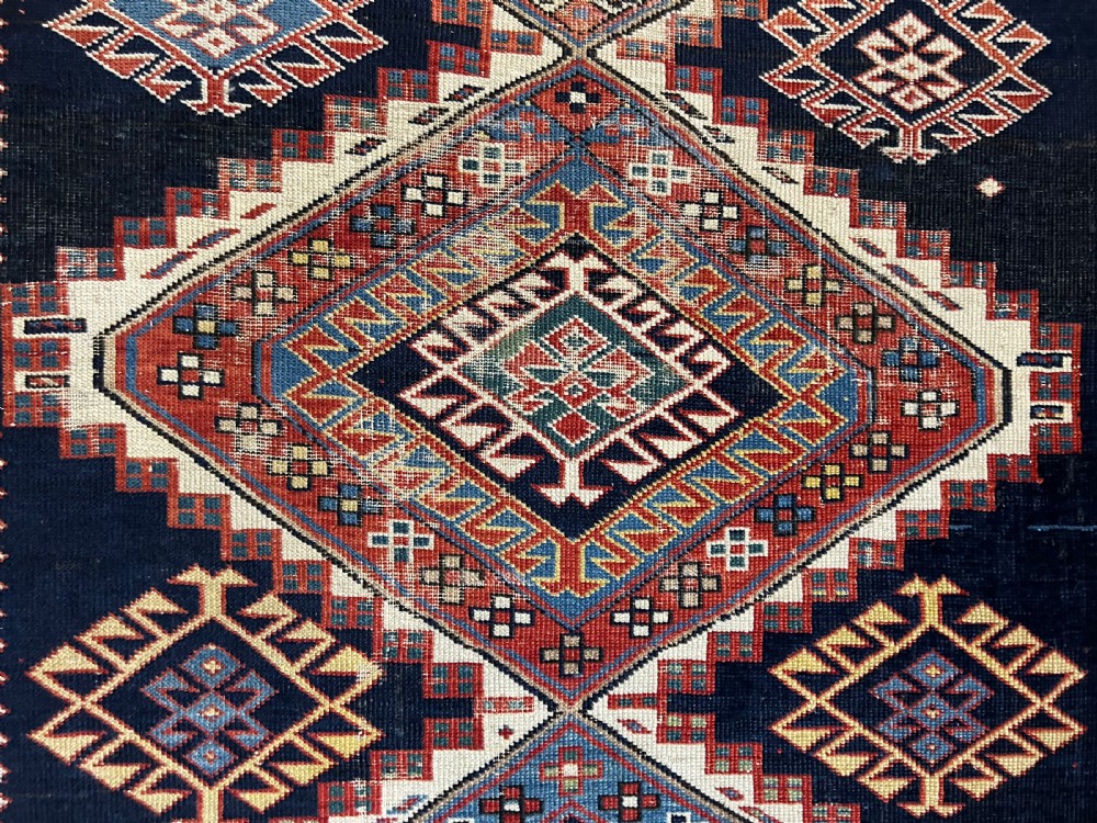 A rectangular hand-knotted wool rug displaying four diamond medallions along a navy central field surrounded by multi-tiered geometric borders. View VI