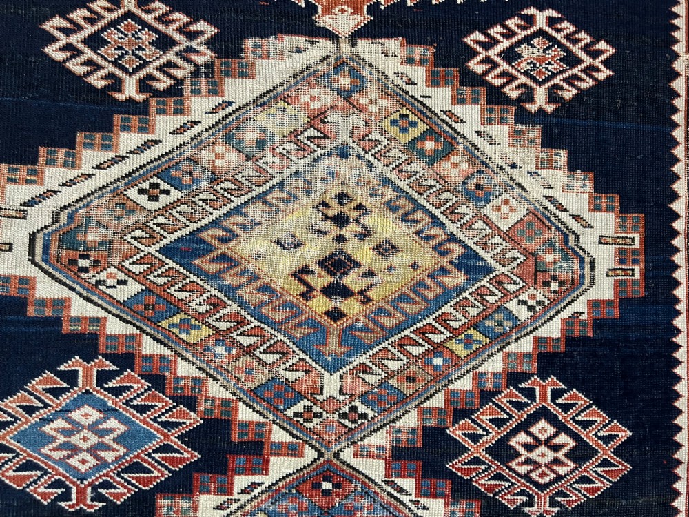 A rectangular hand-knotted wool rug displaying four diamond medallions along a navy central field surrounded by multi-tiered geometric borders. View VII