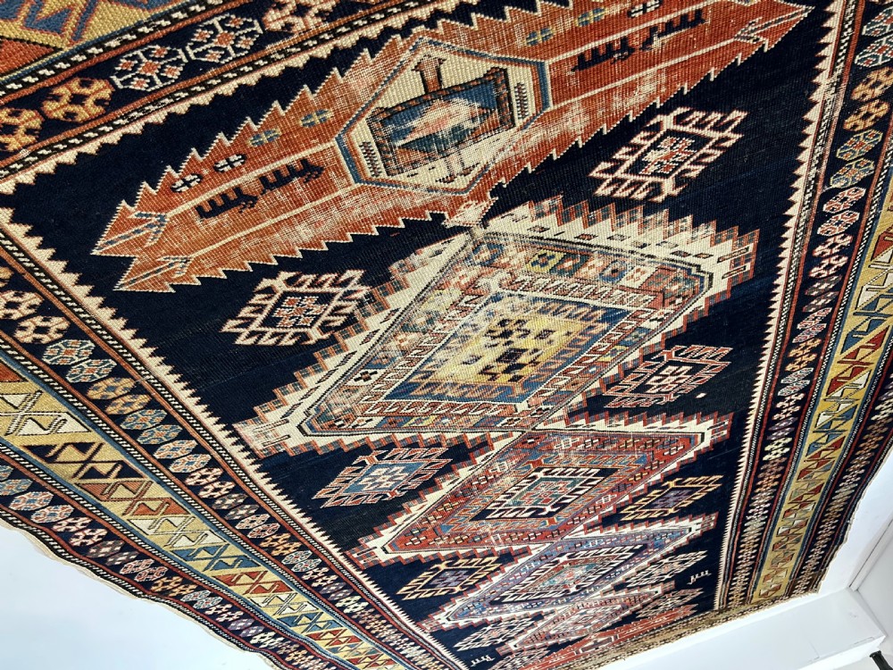 A rectangular hand-knotted wool rug displaying four diamond medallions along a navy central field surrounded by multi-tiered geometric borders. View VIII