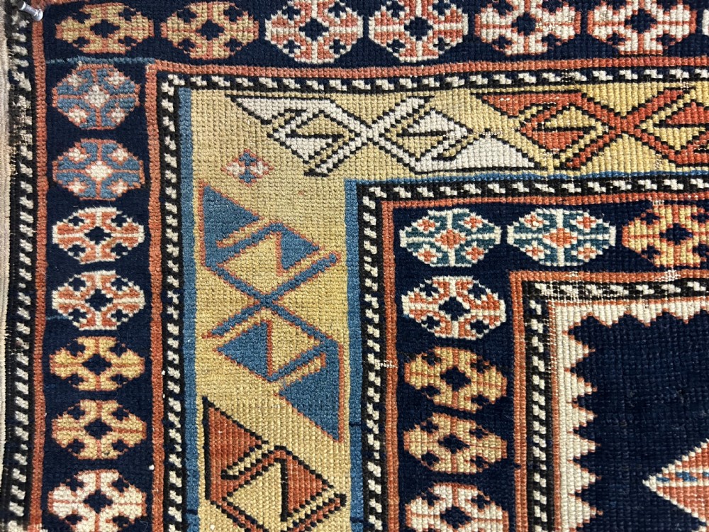 A rectangular hand-knotted wool rug displaying four diamond medallions along a navy central field surrounded by multi-tiered geometric borders. View IX