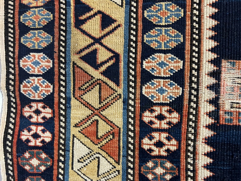 A rectangular hand-knotted wool rug displaying four diamond medallions along a navy central field surrounded by multi-tiered geometric borders. View X