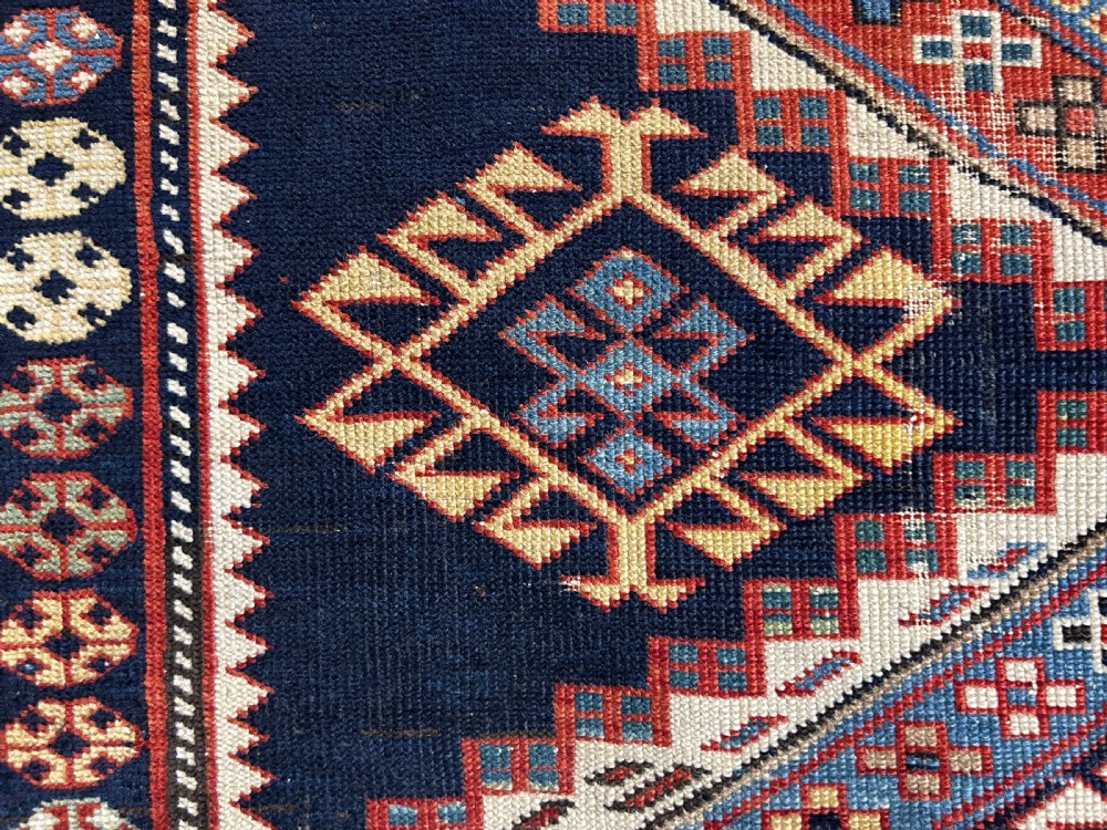 A rectangular hand-knotted wool rug displaying four diamond medallions along a navy central field surrounded by multi-tiered geometric borders. View XI
