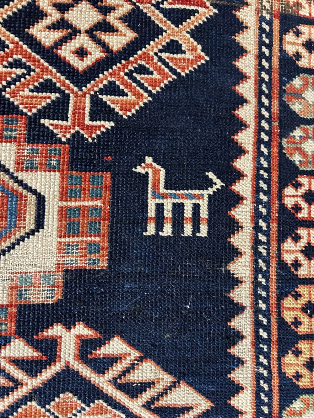 A rectangular hand-knotted wool rug displaying four diamond medallions along a navy central field surrounded by multi-tiered geometric borders. View XIII
