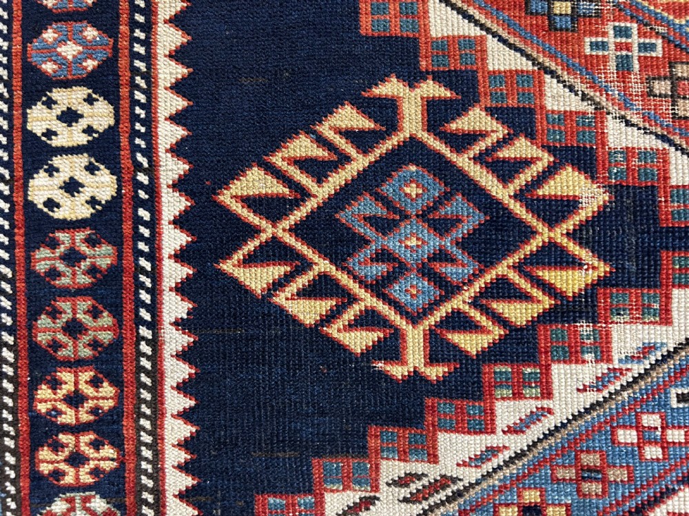 A rectangular hand-knotted wool rug displaying four diamond medallions along a navy central field surrounded by multi-tiered geometric borders. View XIV